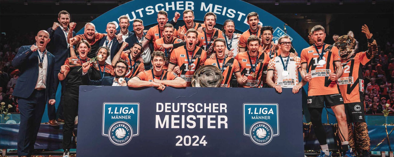 Gruppenfoto der Berlin Recycling Volleys zur Siegerehrung der deutschen Meisterschaft 2024, mit einem Transparent, mehreren Trainern sowie einer Trophäe in den Händen eines Spielers